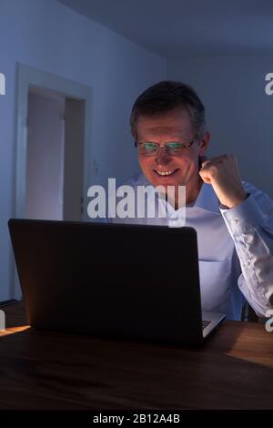 Pleased man working with laptop at night Stock Photo