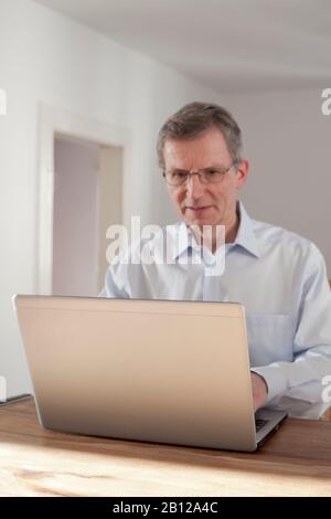 Mature man working with laptop - focus on the edge of the laptop Stock Photo
