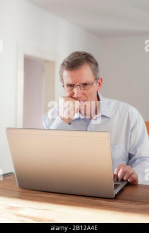 Pensive man working with laptop - focus on the edge of the laptop Stock Photo