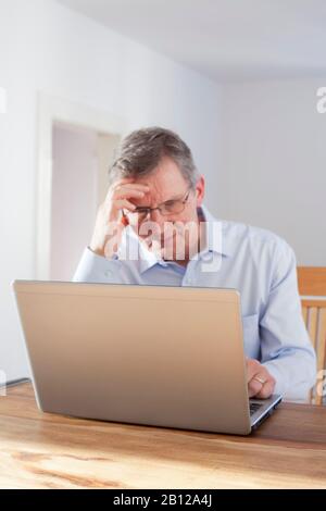 Tired man working with laptop - focus on the edge of the laptop Stock Photo