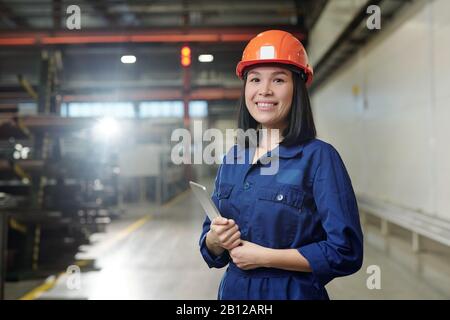 Pretty young smiling engineer in uniform and protective helmet holding tablet Stock Photo