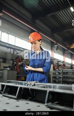 Young serious female engineer in workwear putting on gloves before work Stock Photo