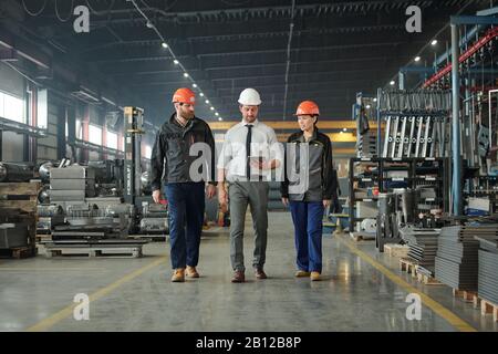 Group of contemporary factory workers in hardhats discussing technical data Stock Photo