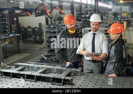 One of three engineers showing his colleagues online data in tablet Stock Photo