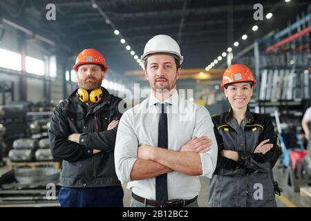 Young foreman in formalwear and hardhat and his two subordinates Stock Photo