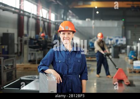 Happy young smiling female engineer in hardhat and blue coveralls Stock Photo