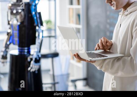 Young man in hoodie using laptop during presentation or testing automation robot Stock Photo
