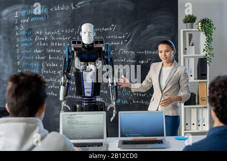Clever young female student showing her classmates new model of automation robot Stock Photo