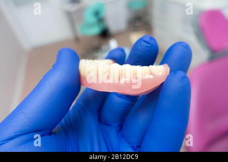 removable denture in the hands of a doctor in blue gloves Stock Photo