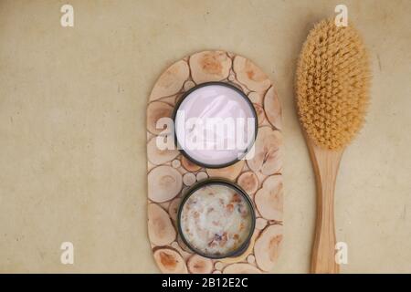 skin care products as pink lotion cream, body brush and salt scrub with rose leaves for peelin. Body care concept. Top view. Copy space Stock Photo