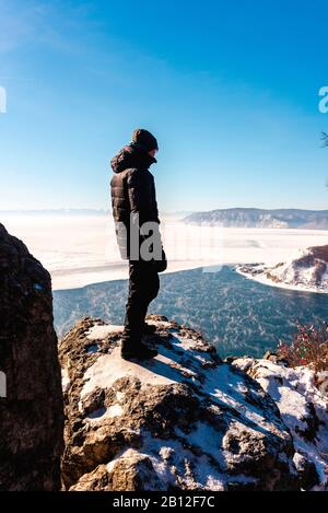 Man stands on a mountain and enjoys the view of the partially frozen Lake Baikal, Siberia, Russia Stock Photo