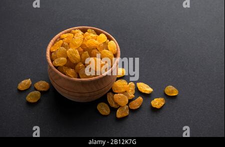 Yellow raisins in wooden bowl on black background