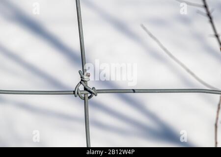 Two metal wires, part of a grid forming an agricultural fence in a farmer's field, intersect with each other, twisting around each other to form a kno Stock Photo