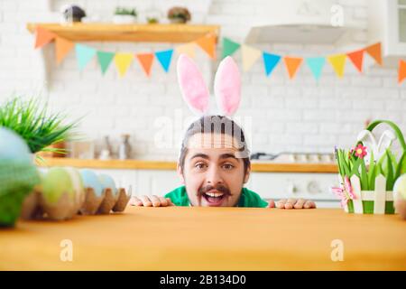 Happy Easter. A funny bearded man with rabbit ears smiling in a decorated room. Stock Photo