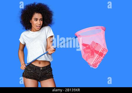 Freestyle. Mulatto girl standing isolated on blue holding butterfly net with gift close-up excited Stock Photo