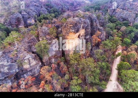 Steep sandstone rocks and cliffs in Australian BLue Mountains over gumtree covered vally and local unsealed road. Lonely girl on the top of the cliff. Stock Photo