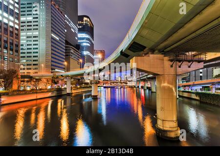 Highway bridge over river in Osaka city CBD at sunrise with bright lights reflecting in waters flowing between skyscrapers. Stock Photo