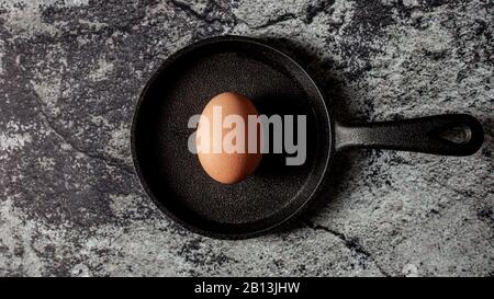 Whole egg in shell on cast iron skillet on concrete background. Dark mood food photography with deep shadows Stock Photo