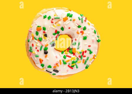 Delicious donuts with white frosting and colorful sprinkles on bright yellow background. Large close up doughnut Stock Photo