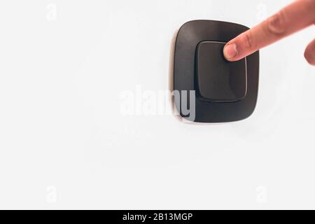 Turning off or turning light switch on wall with finger. Caucasian hand. Contrast picture. White wall and black light switch. Side view Stock Photo