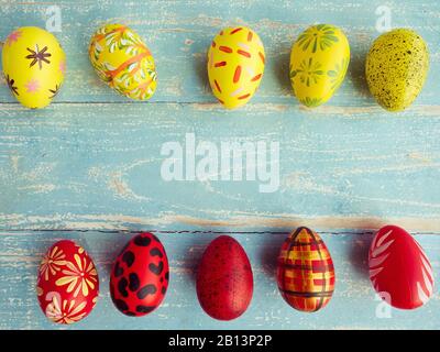 Easter eggs are arranged in two rows between yellow and red on a pastel blue wood floor. Vintage style coloring Stock Photo
