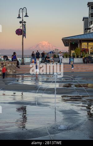 Mt Rainier Hovers Over Downtown Tacoma and Commencement Bay as Seen from Point Ruston with people walking and Riding Bikes Stock Photo