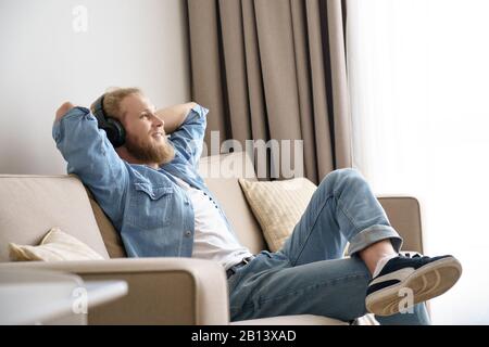 Relaxed young man lounge on sofa wear headphones listening music