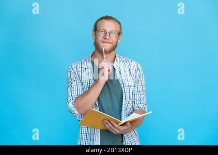Young thoughtful dreamy man hold pen at mouth think plan make notes diary Stock Photo