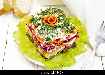 Puff salad with beef, boiled potatoes and beets, pears, spicy Korean carrots, seasoned with mayonnaise and garnished with dill on a green lettuce in p Stock Photo