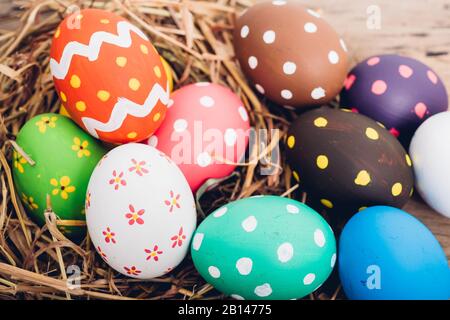 Beautiful Easter multi color egg in straw on wooden background, Easter day concept Stock Photo