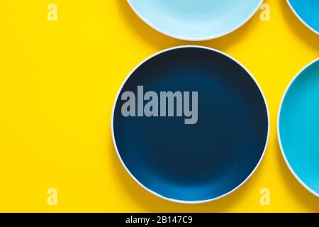 Colorful pastel blue ceramic plates isolated on yellow background. Stock Photo