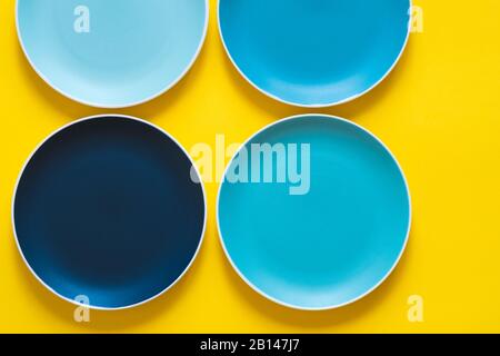 Colorful pastel blue ceramic plates isolated on yellow background. Stock Photo