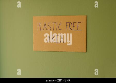 Closeup phrase PLASTIC FREE AREA written on cardboard sign attached on green wall. Climate change, anti-plastic concept Stock Photo