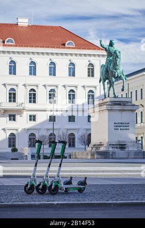 Munich, Germany - February 22, 2020: E-scooters from the company Lime parked in front of Siemens headquarters in Wittelsbacherplatz and the statue of Stock Photo