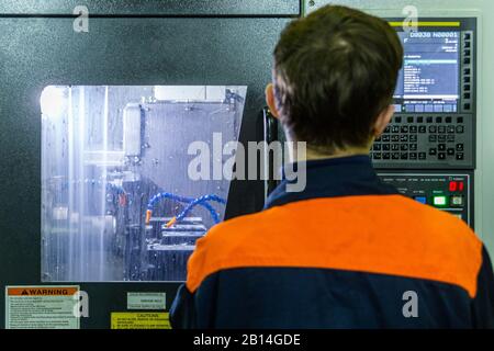 Male operator stands in front of cnc turning machine while working. Close-up with selective focus. Stock Photo