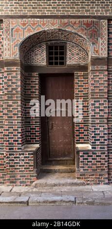 Grunge wooden decorated arched entrance gate with inner small wooden door on wall with black and red bricks with white seam Stock Photo