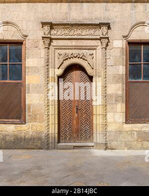 Facade of old abandoned stone decorated bricks wall with arched wooden door and two wooden shutter windows  Stock Photo