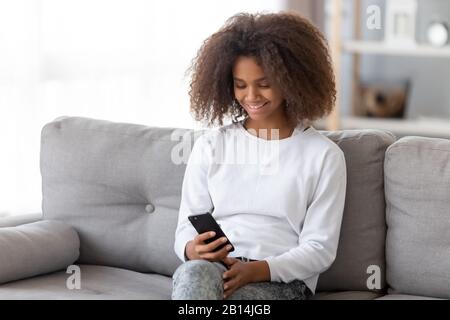 Happy african teen girl holding smartphone using apps at home Stock Photo