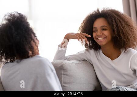 Happy african mother and daughter talking laughing sitting on sofa Stock Photo