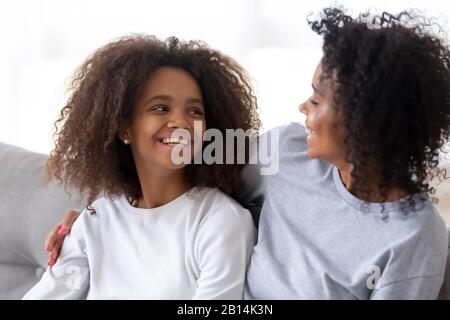 Happy african mom hugging teen daughter laughing talking on sofa Stock Photo