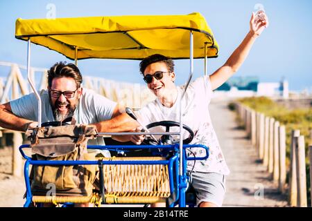 Father and son friends have fun together laughing a lot on a vehicle bike - crazy mixed generations people enjoy the vacation and life - craziness and Stock Photo
