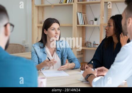 Concentrated young mixed race colleagues listening to female team leader. Stock Photo