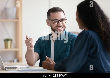 Smiling young man chatting with mixed race female colleague. Stock Photo