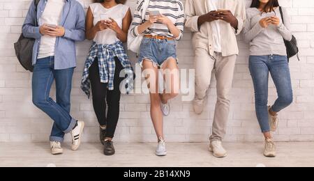 Cropped of multiethnic friends uisng smartphones, leaning on white wall Stock Photo