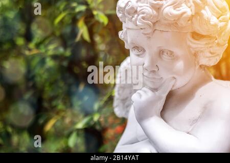 Garden decorate background concept. White vintage statue cupid in the garden with green copy space at the left side. Morning light , bokeh and lens fl Stock Photo