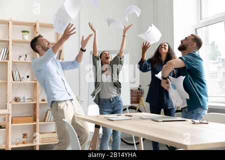 Overjoyed young multiracial business team throwing paper documents in air. Stock Photo