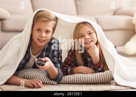Happy Girl And Boy Watching TV Lying On Floor Indoor Stock Photo