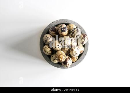 Quail Easter eggs and feathers in ceramic bowl on white background. Natural healthy food and organic farming, easter and spring concept. Stock Photo