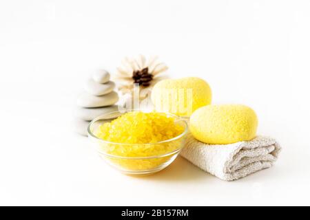 Relaxing bath products composition with yellow heart shaped bath bombs, sea salt scrab, flower, towel and stone stack on a light background. Relaxation, spa and body treatment concept. Stock Photo