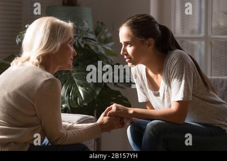 Side view two generations sitting opposite each other, holding hands. Stock Photo